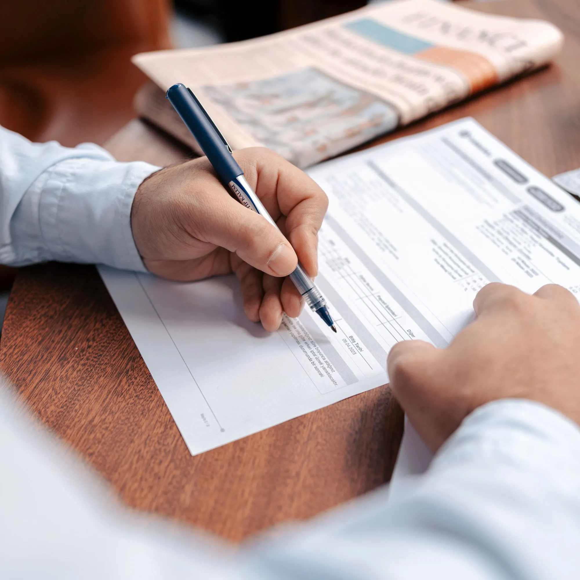 A hand filling in a printed form with a pen.